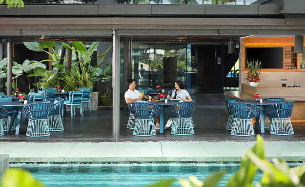 A waitress serving drinks and pizza in a pool-side restaurant to a customer with  beautiful pool and garden view in Semarang