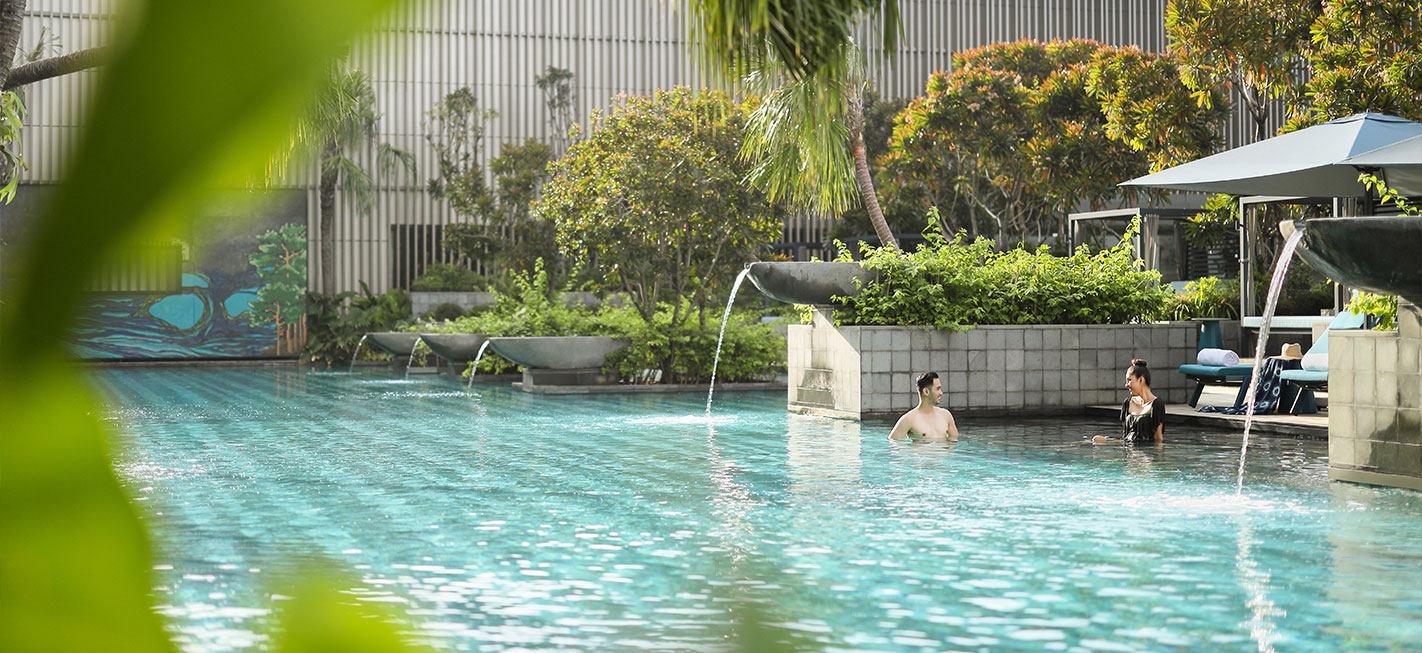 Couple smiling in a heated pool around garden in front of pool access room at Padma Hotel Semarang